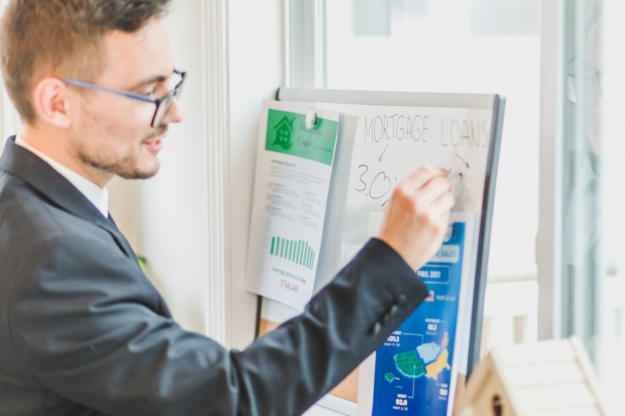 Businessman in suit writes on whiteboard displaying mortgage loan rates during a real estate meeting.